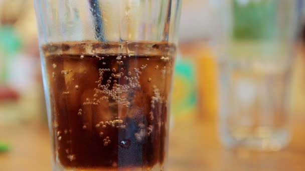 Vaso con cola y hielo sobre una mesa — Vídeo de stock