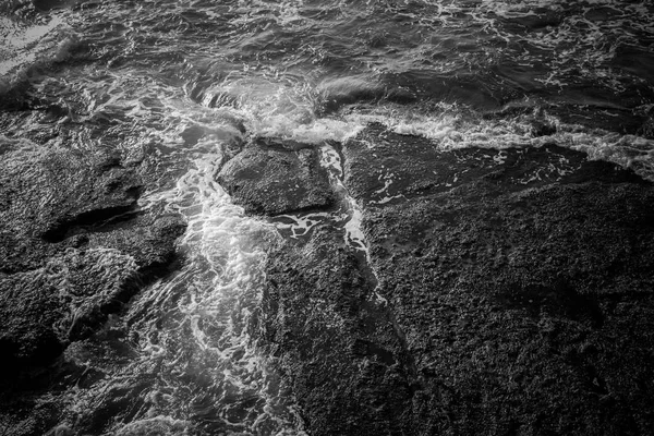 White sea foam and black rocks surface