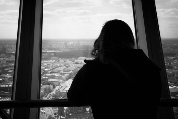 Silhouette of back view of woman looking out of a window at the berlin city skyline. View from inside of the tv tower building.
