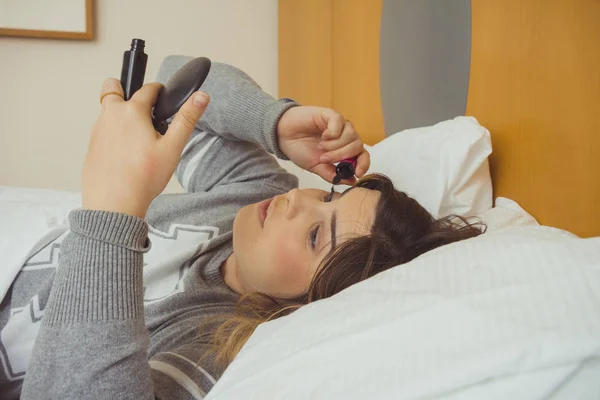 Donna che applica il trucco mentre è sdraiata sul suo letto — Foto Stock