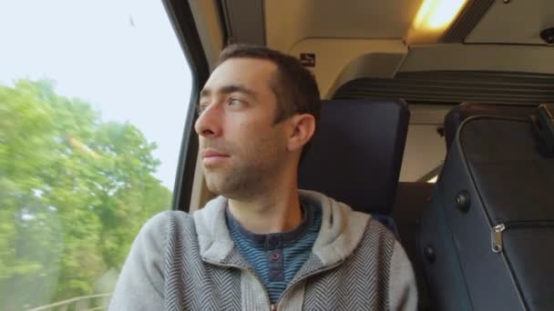 Jongeman in een trein reizen en kijkt uit het raam — Stockvideo
