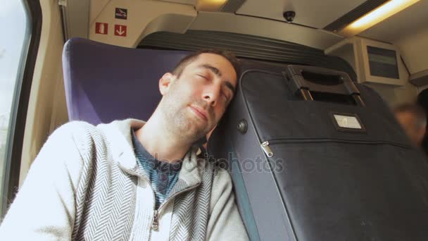 Young man traveling on a train and sleep on blue suitcase next to him — Stock Video