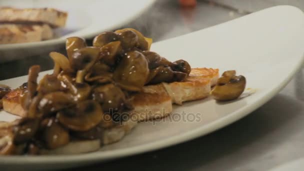 Kocken förbereder en maträtt med svamp i en sås toppad på rostad fisk på vit platta — Stockvideo