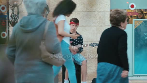 Jerusalém, Israel - 11 de maio de 2017: Jovem músico de rua guitarrista toca música perto de moedas de dinheiro em caixa de guitarra na frente de pessoas transeuntes na rua comercial Mamilla shopping ao ar livre em Jerusalém — Vídeo de Stock