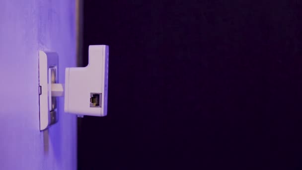 人は壁の電気ソケットにあるWiFiエクステンダー装置にイーサネットケーブルを挿入する。このデバイスは、家庭やオフィスでワイヤレスネットワークを拡張するのに役立つアクセスポイントモードです。. — ストック動画