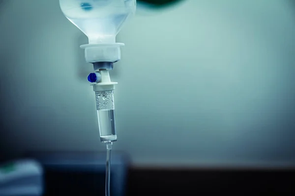 Set IV fluid intravenous drop saline drip in a hospital room. Close up, dark blue light background, selective focus and copy space.