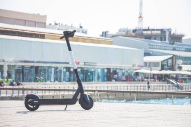 Güneşli bir yaz gününde Tel Aviv Limanı ticari bölgesinde bir güvertede siyah elektrikli scooter park ediyor. Seçici odağı kopyalama alanı ile kapat.