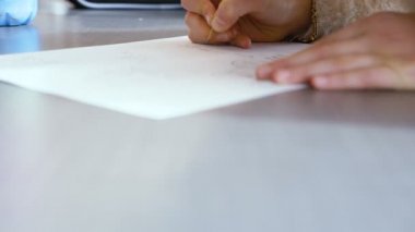 Küçük İsrailli beyaz yetenekli kız bir ilkokul sınıfında not defterine yazıyor. Egzersizi çözmeye ve cevaplarını kağıda yazmaya çalışıyor. Ellerine ve kalemine yakın dur..