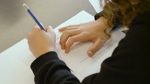 イスラエル人の白人の10代の少女が小学校のクラスでテストを受けています 彼女は試験を解決し 論文で答えを書こうとする 彼女の手とペンで — ストック動画