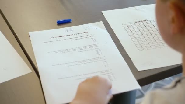 イスラエルの白人の10代の天才少年が小学校のクラスでテストを受けています 彼は試験を解決し 論文で答えを書こうとする 彼の手とペンを閉じて — ストック動画