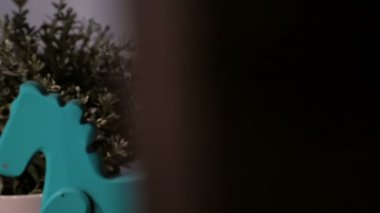 Minyatür ahşap sallanan at oyuncağı ve tahta bir rafta saksı. Çocukluk dekoratif oyuncaklarına yaklaş. Açığa vurarak sola dönüyor. Seçici odak.