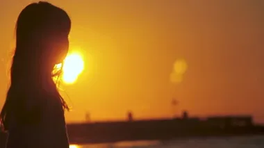 Kaygısız, tanınmayan bir kızın gölgesinin arkası egzotik bir günbatımının güzel bir manzarasının keyfini çıkarıyor. Sahilde güneşe doğru duruyor. İsrail, Tel Aviv 'de altın gün doğumu.