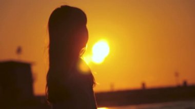 Kaygısız, tanınmayan bir kızın gölgesinin arkası egzotik bir günbatımının güzel bir manzarasının keyfini çıkarıyor. Sahilde güneşe doğru duruyor. İsrail, Tel Aviv 'de altın gün doğumu.
