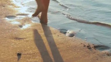 Tasasız, tanınmayan bir kız, egzotik gün batımında sığ okyanus dalgalarıyla karşılaşır. Tropikal bir plajda bacaklarındaki yakın çekim altın gündoğumunda ferahlatıcı denize doğru koşar. Kumda ayak izleri..
