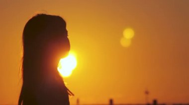 Tasasız kızın sineması, rüzgarda savrulan saçlarıyla egzotik bir günbatımının tadını çıkarıyor. Tel Aviv 'de altın gündoğumunda tropikal bir sahilde dikilirken çekilmiş bir silueti..