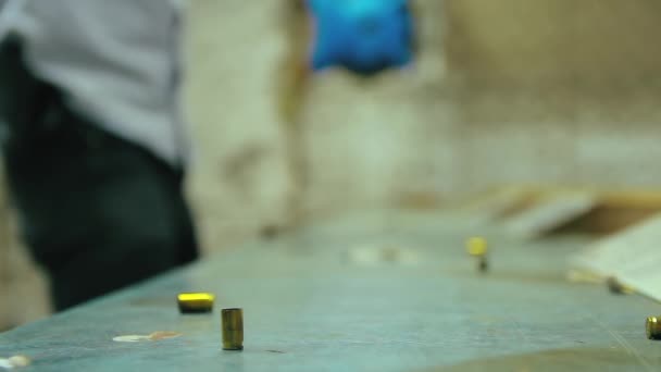 空のピストル銃弾の砲弾が落下し 撮影範囲内の木製のテーブルに影響を与えるシネマグラフ 男は9Mm砲を背景に射撃している ループ 選択フォーカス コピースペース — ストック動画