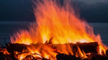 Alacakaranlıkta sahilde bir kamp ateşinin sineması. Ateşe kıvılcımlar ve sıcak hava dalgalarıyla yaklaş..