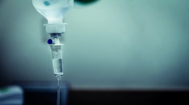 Hastane odasında damardan akan sıvı salin damlalarının sinemagrafı. Koyu mavi ışık arkaplanındaki damardan sıvı damlası tuzuna yaklaş. Döngü, seçici odak ve boşluğu kopyala.