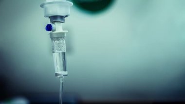 Hastane odasında damardan akan sıvı salin damlalarının sinemagrafı. Koyu mavi ışık arkaplanındaki damardan sıvı damlası tuzuna yaklaş. Döngü, seçici odak ve boşluğu kopyala.