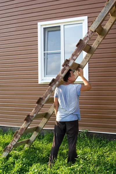 Мужчина приставляет к дому деревянную лестницу — стоковое фото