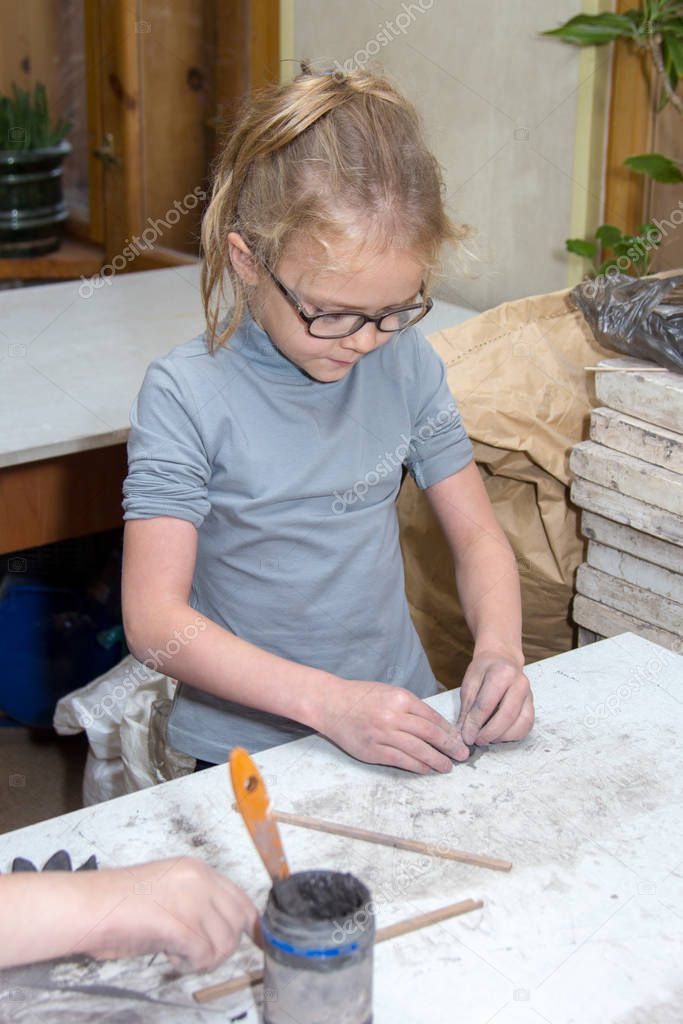 little girl in glasses sculpts clay
