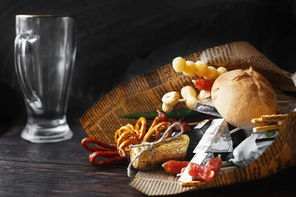 a can of beer with a snack on a wooden dark background with an empty beer glass. gift bouquet to a man