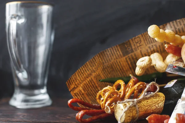 a can of beer with a snack on a wooden dark background with an empty beer glass. gift bouquet to a man