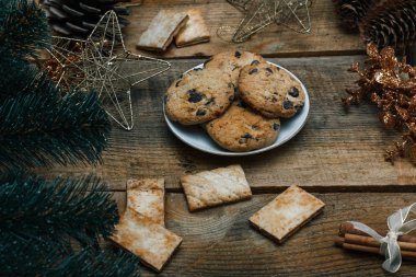 Çikolata kurabiye ahşap arka plan üzerinde beyaz bir tabak içinde. Çevre koniler ve tarçın sopa, kabaca. Yukarıdan görüntüleyin. Yeni yıl tatili Tema