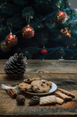 Çikolatalı kurabiye rustik arka plan üzerinde. Yakındaki yalan tarçın sopa ve konileri. Oyuncaklar ve çelenk ile ağacı gerisindedir. Yeni yıl tatili.