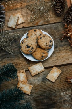 Çikolata kurabiye ahşap arka plan üzerinde beyaz bir tabak içinde. Çevre koniler ve tarçın sopa, kabaca. Yukarıdan görüntüleyin. Yeni yıl tatili Tema
