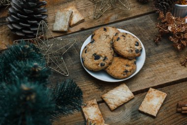 Çikolata kurabiye ahşap arka plan üzerinde beyaz bir tabak içinde. Çevre koniler ve tarçın sopa, kabaca. Yukarıdan görüntüleyin. Yeni yıl tatili Tema