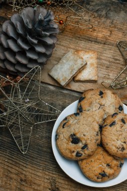 Çikolata kurabiye ahşap arka plan üzerinde beyaz bir tabak içinde. Çevre koniler ve tarçın sopa, kabaca. Yukarıdan görüntüleyin. Yeni yıl tatili Tema