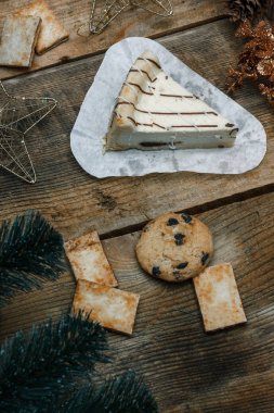 Ahşap arka plan üzerinde beyaz kağıt üzerinde güzel ev yapımı pasta peynirli kek. Sonraki çikolatalı kurabiye, Noel hediyeleri, yılbaşı ağacı, koni ve oyuncaklar. Yılbaşı kutlamak için gebe.