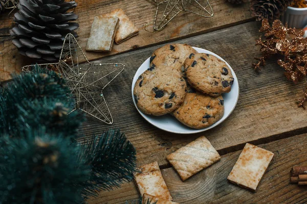 Çikolata kurabiye ahşap arka plan üzerinde beyaz bir tabak içinde. Çevre koniler ve tarçın sopa, kabaca. Yukarıdan görüntüleyin. Yeni yıl tatili Tema