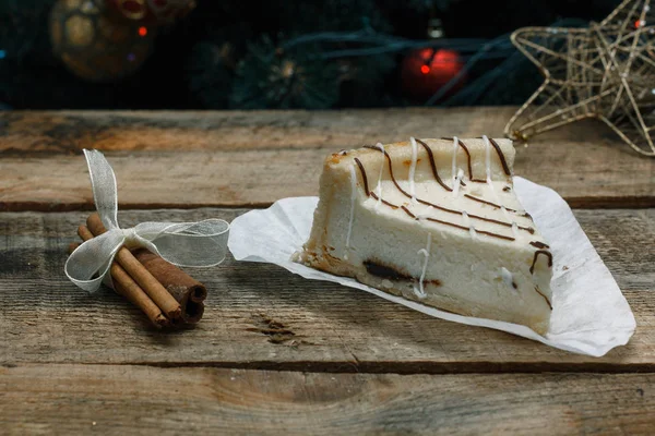 Güzel ev yapımı pasta peynirli kek tarçın çubuğu ile ahşap arka plan üzerinde beyaz kağıt üzerinde. Noel hediyeler, Noel ağacı ve oyuncaklar. Yılbaşı kutlamak için gebe.