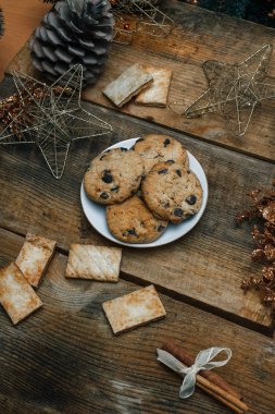 Çikolata kurabiye ahşap arka plan üzerinde beyaz bir tabak içinde. Çevre koniler ve tarçın sopa, kabaca. Yukarıdan görüntüleyin. Yeni yıl tatili Tema