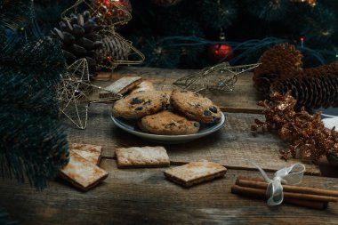 Güzel genel kavram. Çikolata kurabiye ahşap arka plan üzerinde beyaz bir tabakta. Yakın bir Noel ağacı, oyuncak, çelenk ve Noel oyuncaklar standları.