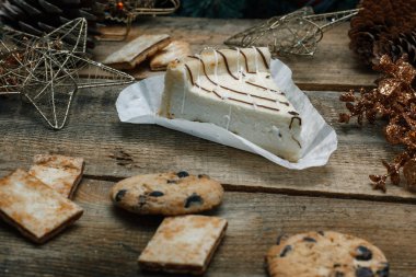 Ahşap arka plan üzerinde beyaz kağıt üzerinde güzel ev yapımı pasta peynirli kek. Sonraki çikolatalı kurabiye, Noel hediyeleri, yılbaşı ağacı, koni ve oyuncaklar. Yılbaşı kutlamak için gebe.