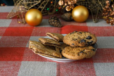 Damalı bir masa örtüsü ahşap arka plan üzerinde beyaz bir tabağa çikolatalı çerezleri. Çevre koniler ve tarçın sopa, kabaca. Yeni yıl tatili Tema