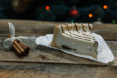 Güzel ev yapımı pasta peynirli kek tarçın çubuğu ile ahşap arka plan üzerinde beyaz kağıt üzerinde. Noel hediyeler, Noel ağacı ve oyuncaklar. Yılbaşı kutlamak için gebe.