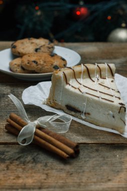 Güzel ev yapımı pasta peynirli kek tarçın çubuğu ile ahşap arka plan üzerinde beyaz kağıt üzerinde. Noel hediyeler, Noel ağacı ve oyuncaklar. Yılbaşı kutlamak için gebe.