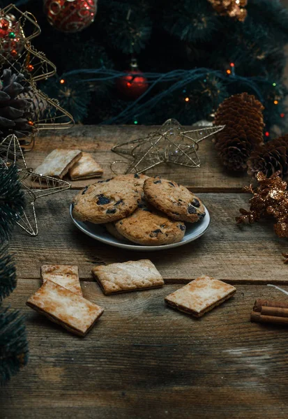 Belo conceito. Biscoitos de chocolate em uma chapa branca em um fundo de madeira. Perto fica uma árvore de Natal, brinquedos, guirlandas e brinquedos de Natal . — Fotografia de Stock