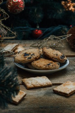 Güzel genel kavram. Çikolata kurabiye ahşap arka plan üzerinde beyaz bir tabakta. Yakın bir Noel ağacı, oyuncak, çelenk ve Noel oyuncaklar standları.
