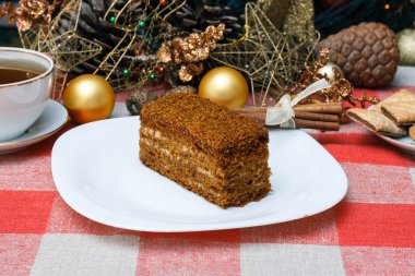 Damalı bir masa örtüsü ile çay, bisküvi, tarçın bir yılbaşı Noel ağacı bir arka plan üzerinde beyaz bir tabağa kek. Yeni konsept. Tatil için.