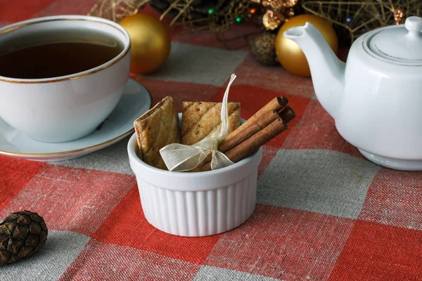 Chocolate cookies and cinnamon sticks on a white plate on a checkered tablecloth on the background of Christmas tree. Concepts of the New Year holiday. For holiday. — Stock Photo, Image