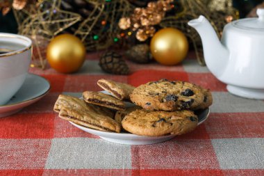 Damalı bir masa örtüsü ahşap arka plan üzerinde beyaz bir tabağa çikolatalı çerezleri. Çevre koniler ve tarçın sopa, kabaca. Yeni yıl tatili Tema