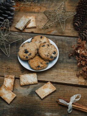 Çikolata kurabiye ahşap arka plan üzerinde beyaz bir tabak içinde. Çevre koniler ve tarçın sopa, kabaca. Yukarıdan görüntüleyin. Yeni yıl tatili Tema