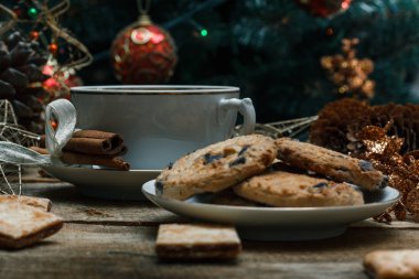 Güzel genel kavram. Çikolata kurabiye ve çay bir ahşap arka plan beyaz tabakta. Yakın bir Noel ağacı, oyuncak, çelenk ve Noel oyuncaklar standları.