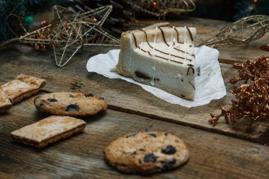 Ahşap arka plan üzerinde beyaz kağıt üzerinde güzel ev yapımı pasta peynirli kek. Sonraki çikolatalı kurabiye, Noel hediyeleri, yılbaşı ağacı, koni ve oyuncaklar. Yılbaşı kutlamak için gebe.