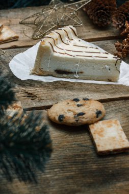 Ahşap arka plan üzerinde beyaz kağıt üzerinde güzel ev yapımı pasta peynirli kek. Sonraki çikolatalı kurabiye, Noel hediyeleri, yılbaşı ağacı, koni ve oyuncaklar. Yılbaşı kutlamak için gebe.